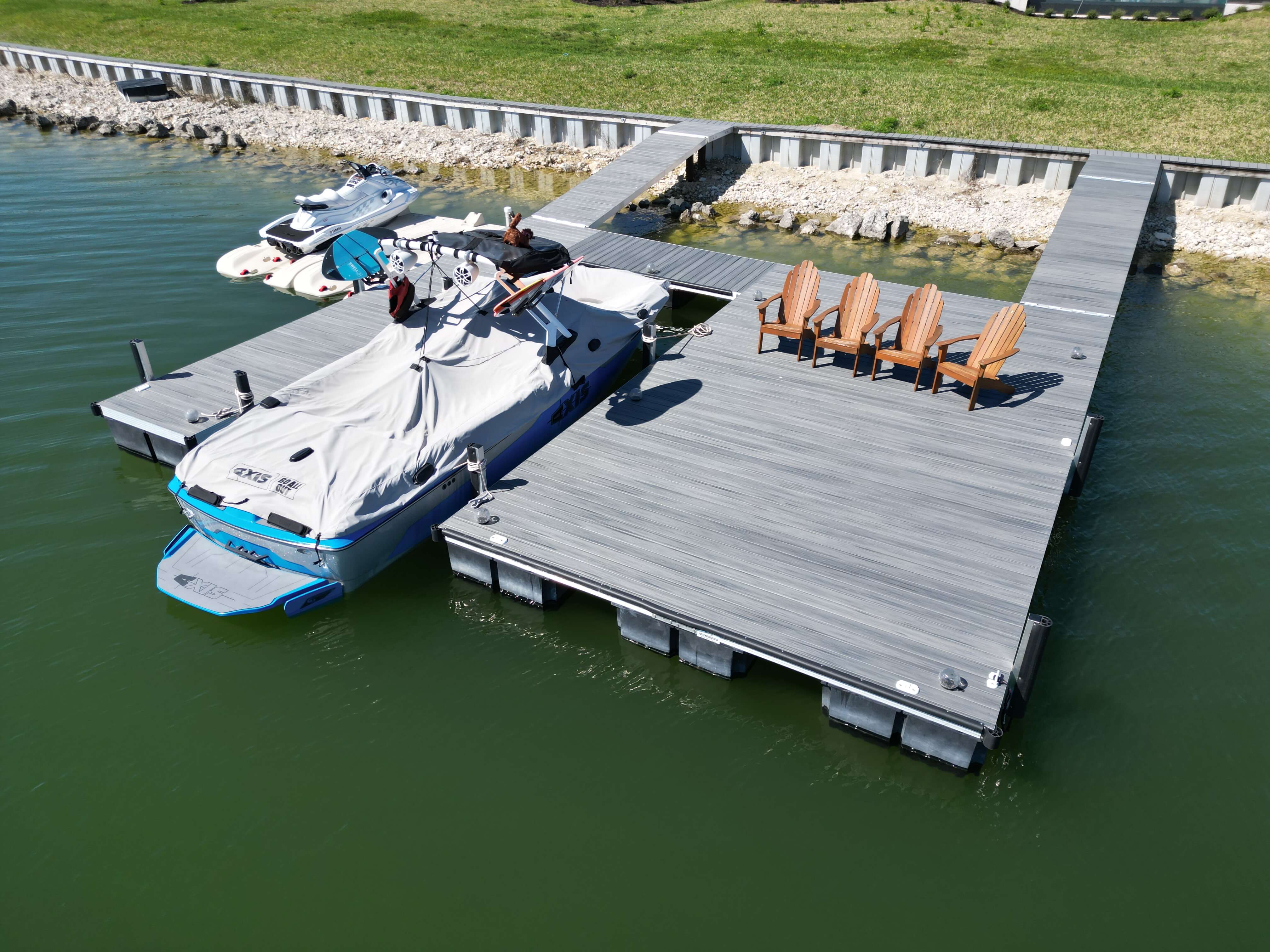 Floating dock with boat lift area, covered boat, jet skis, and seating on a waterfront dock.