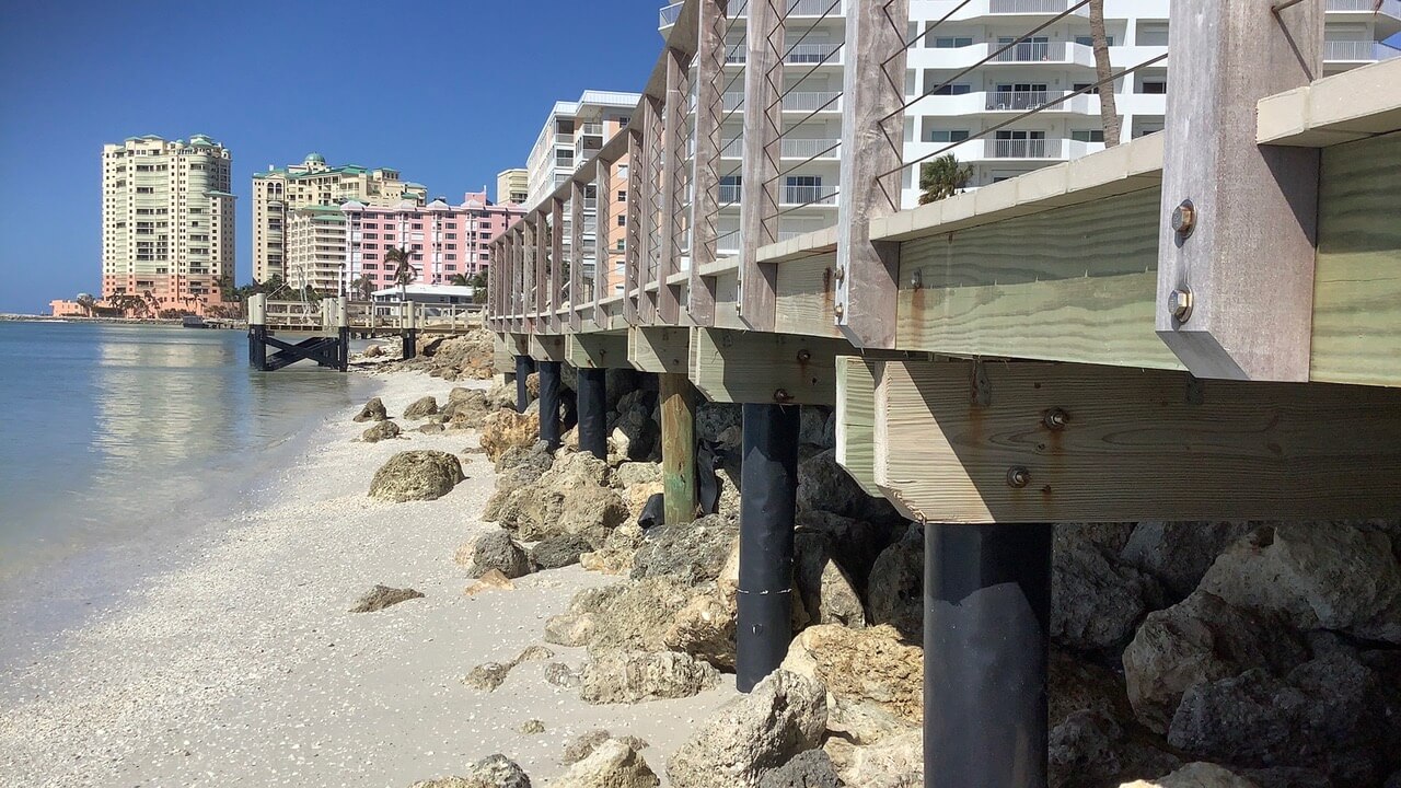 Waterfront dock construction project beside a rocky shoreline with buildings in the background